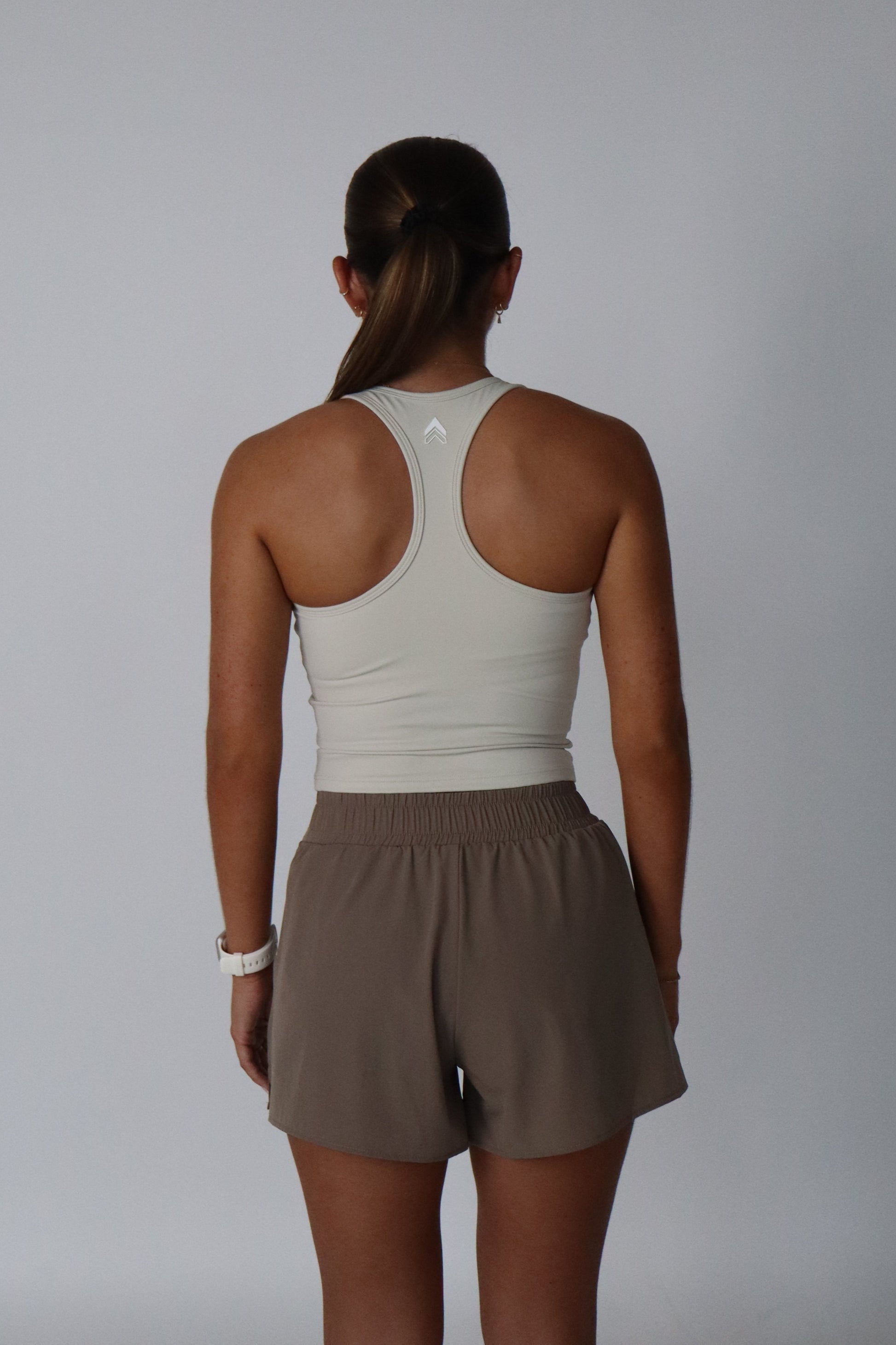 Person wearing a beige tank top and brown shorts on a plain background